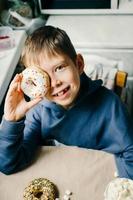 grappig jongen met donut. kind is hebben pret met donut. smakelijk voedsel voor kinderen. gelukkig tijd Bij huis met zoet voedsel. foto