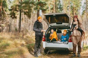 een familie met twee kinderen zijn zittend Aan een picknick in de bossen, in de romp van een auto. familie en knus wandelingen in de Woud. op reis in winter en herfst door auto. wandelen gedurende de coronavirus foto