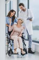 dokter en verpleegster zorgzaam hun senior vrouw geduldig in rolstoel Bij verpleging huis foto