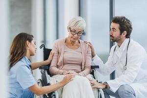 dokter en verpleegster pratend met hun senior vrouw rolstoelgebonden geduldig Bij de ziekenhuis foto