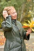 een ouderen vrouw in een herfst park verzamelt een boeket van geel esdoorn- bladeren. foto