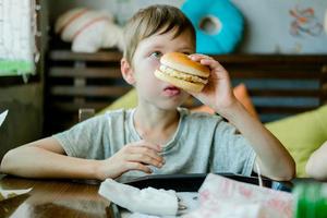 jongen aan het eten een groot hamburger met een kotelet. Hamburger in de handen van een kind. heerlijk en bevredigend kip kotelet hamburger. afhaalmaaltijd voedsel foto