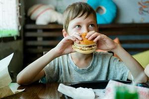 jongen aan het eten een groot hamburger met een kotelet. Hamburger in de handen van een kind. heerlijk en bevredigend kip kotelet hamburger. afhaalmaaltijd voedsel foto