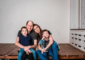 glimlachen familie Holding huis vorm terwijl zittend Aan hardhout verdieping Bij huis. fotoshoot van een familie met 2 zonen, wit achtergrond. warm familie verhoudingen. jong ouders foto