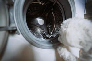 schattig weinig wit hond op zoek in naar het wassen machine. foto