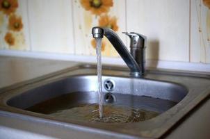 roestvrij staal wastafel plug gat dichtbij omhoog vol van water en deeltjes van voedsel foto