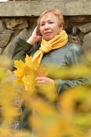 een ouderen vrouw in een herfst park verzamelt een boeket van geel esdoorn- bladeren. foto