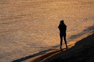 achtergrondverlichting van een silhouet van een anoniem vrouw nemen foto's in de zee foto