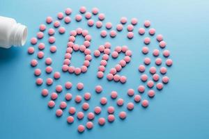 roze tablets in de het formulier van b12 in de hart Aan een blauw achtergrond, gemorst van een wit kan. foto