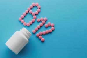 roze pillen in de vorm van de brief b12 Aan een blauw achtergrond, gemorst uit van een wit kan, laag contrast foto