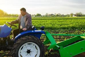 boer schijven trekker aan de overkant boerderij veld. oogst eerste aardappelen in vroeg de lente. landbouw en landbouwgrond. agro industrie en landbouwbedrijf. oogsten mechanisatie in ontwikkelen landen. boerderijen ondersteuning foto