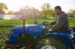 een boer Aan een trekker schijven aan de overkant de boerderij veld. agro industrie, landbouwbedrijf. aardappel oogst campagne. landbouw, landbouw. oogsten aardappelen in vroeg de lente. platteland landbouwgrond. foto