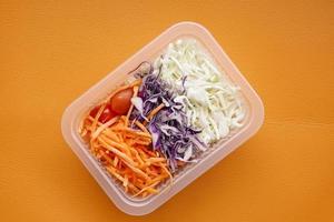 vers groente salade in een plastic houder Aan oranje achtergrond foto
