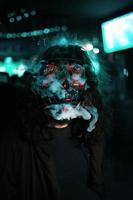 Mens in kap met lang verward haar- in een verlichting neon gloeiend masker. foto