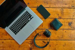 laptop, draadloze koptelefoon, mobiel telefoon, en portemonnee Aan houten tafel. foto