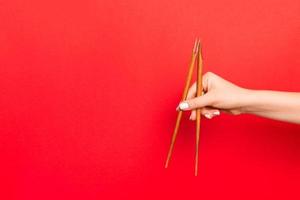 houten eetstokjes vastgehouden met vrouw handen Aan rood achtergrond. klaar voor aan het eten concepten met leeg ruimte foto