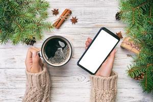 vrouw handen Holding modern smartphone met moskee omhoog en mok van koffie Aan houten rustiek wijnoogst tafel met Kerstmis decoratie. top visie foto