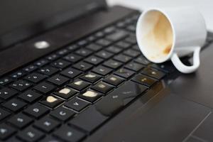 morsen koffie van wit kop Aan de computer laptop toetsenbord vloeistof foto