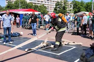 een brandweerman in een vuurvast pak en een helm rennen met een zuurstof ballon trekken, Holding een brand slang Bij een brand sport wedstrijd. Minsk, Wit-Rusland, 08.07.2018 foto