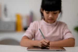 Aziatisch weinig schattig meisje aanraken de digitaal tablet scherm Aan de tafel foto