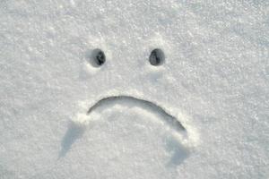 verdrietig smiley gezicht getrokken in de sneeuw Aan een zonnig winter dag. kopiëren ruimte. negatief emoties. foto