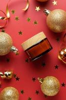 creatief nieuw jaar en Kerstmis presentatie van schoonheidsmiddelen verpakking. amber glas merkloos room pot met schitteren goud kerstballen, confetti Aan rood achtergrond. modieus mockup voor u merk foto