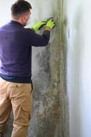 de Mens toepassingen een spatel naar verwijderen gietvorm en schimmel Aan de muur. foto