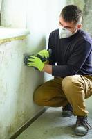 schimmel en gietvorm is een manifestatie van overschot vochtigheid in de kamer, een Mens met een spatel verwijdert schimmel en gietvorm van de muur. foto