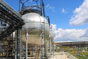 een groot ronde kogelvormig glimmend metalen hoge druk ijzer opslagruimte tank voor ammoniak is sterk met pijpen en uitrusting Bij de petrochemisch chemisch raffinaderij industrieel raffinaderij foto