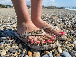 vrouw poten, voeten in rubber slippers met een mooi rood pedicure Aan de achtergrond van zand Aan vakantie Aan de strand in een warm tropisch oostelijk paradijs land zuidelijk toevlucht foto