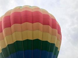 groot veelkleurig helder ronde regenboog gekleurde gestreept gestreept vliegend ballon met een mand tegen de lucht in de avond foto