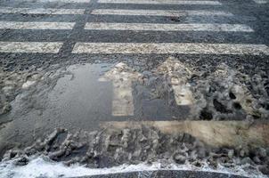 zebrapad met pijlen wijzend op verkeer, voor veiligheid Aan de weg. voetganger kruispunt en snelweg markeringen in de vuil smelten sneeuw. foto