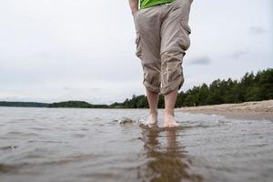 blootsvoets mannetje poten in gerold omhoog broek staan rustig Aan de zanderig onderkant, in de water van de meer. levensstijl. bodem visie. foto