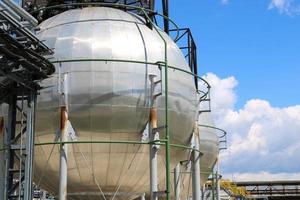 een groot ronde kogelvormig glimmend metalen hoge druk ijzer opslagruimte tank voor ammoniak is sterk met pijpen en uitrusting Bij de petrochemisch chemisch raffinaderij industrieel raffinaderij foto