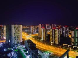 visie van de nacht stad van een hoogte. hoog huizen met panoramisch ramen en geschilderd gevels. De volgende naar een bezig weg voor voetgangers en auto's foto