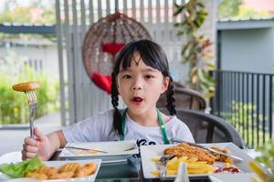 Aziatisch jong meisje Aziatisch eten gebakken ei Aan schotel Bij tafel. foto