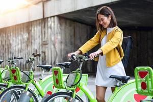 stad fiets - Aziatisch vrouw gebruik makend van openbaar stad fietsen sharing systeem. fietsen vrouw professioneel parkeren stad Fietsen na wielersport Aan stad fiets. foto