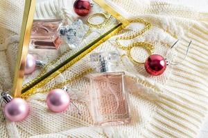 een fles van vrouwen parfum is weerspiegeld in een spiegel met Kerstmis ballen. gebreid beige achtergrond. geschenk begrip, geur presentatie. foto