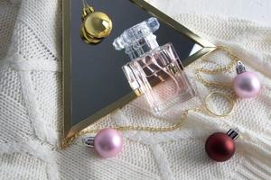 een chique fles van parfum met een bloemen aroma tegen de achtergrond van een spiegel, ballen en een gebreid trui. de concept van een nieuw jaar geschenk. foto