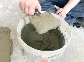 bouwer handen met een metaal spatel kneedt in een groot wit plastic bouw emmer gips, tegel lijm, cement voor de reparatie van een appartement, huis, nivelleren de muren foto