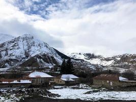 klein steen huizen, gebouwen in de dorp Aan een mooi berg verkoudheid winter toevlucht met hoog berg pieken de nevel en sneeuw gedekt rotsen voor snowboarden en skiën tegen een blauw lucht foto