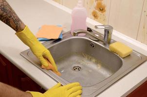 persoon of gezinshoofd schoonmaak de keuken wastafel met spons in dichtbij omhoog visie foto