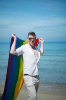 jong homo Mens Holding regenboog vlaggen terwijl staand Aan de strand foto