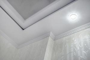 detail van hoek plafond met ingewikkeld kroon vormen. geschorst plafond en gipsplaat bouw in leeg kamer in appartement of huis. rekken plafond wit en complex vorm geven aan. foto