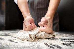 sterk handen van een bakker kneden deeg Aan een bebloemd tafel. brood maken. foto