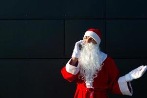 modern de kerstman claus pratend Aan de telefoon. bestellen de Diensten van een animator voor de Kerstmis en nieuw jaar. online groeten via de internet en mobiel communicatie, sociaal afstand foto