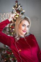 een blond vrouw in een rood trainingspak in de buurt een Kerstmis boom. slinger ster in de buurt de gezicht. kerstmis, nieuw jaar, vakantie verzinnen, detailopname portret foto