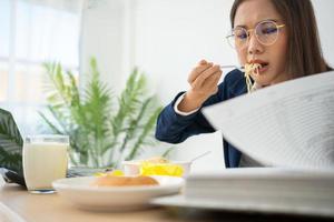 bezig en moe zakenvrouw aan het eten spaghetti voor lunch Bij de bureau kantoor en werken naar leveren financieel verklaringen naar een baas. overwerkt en ongezond voor klaar maaltijden, burn-out concept. foto