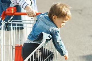 schattig weinig jongen zittend in een boodschappen doen kar foto