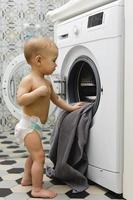 schattig baby jongen is op zoek binnen de het wassen machine foto